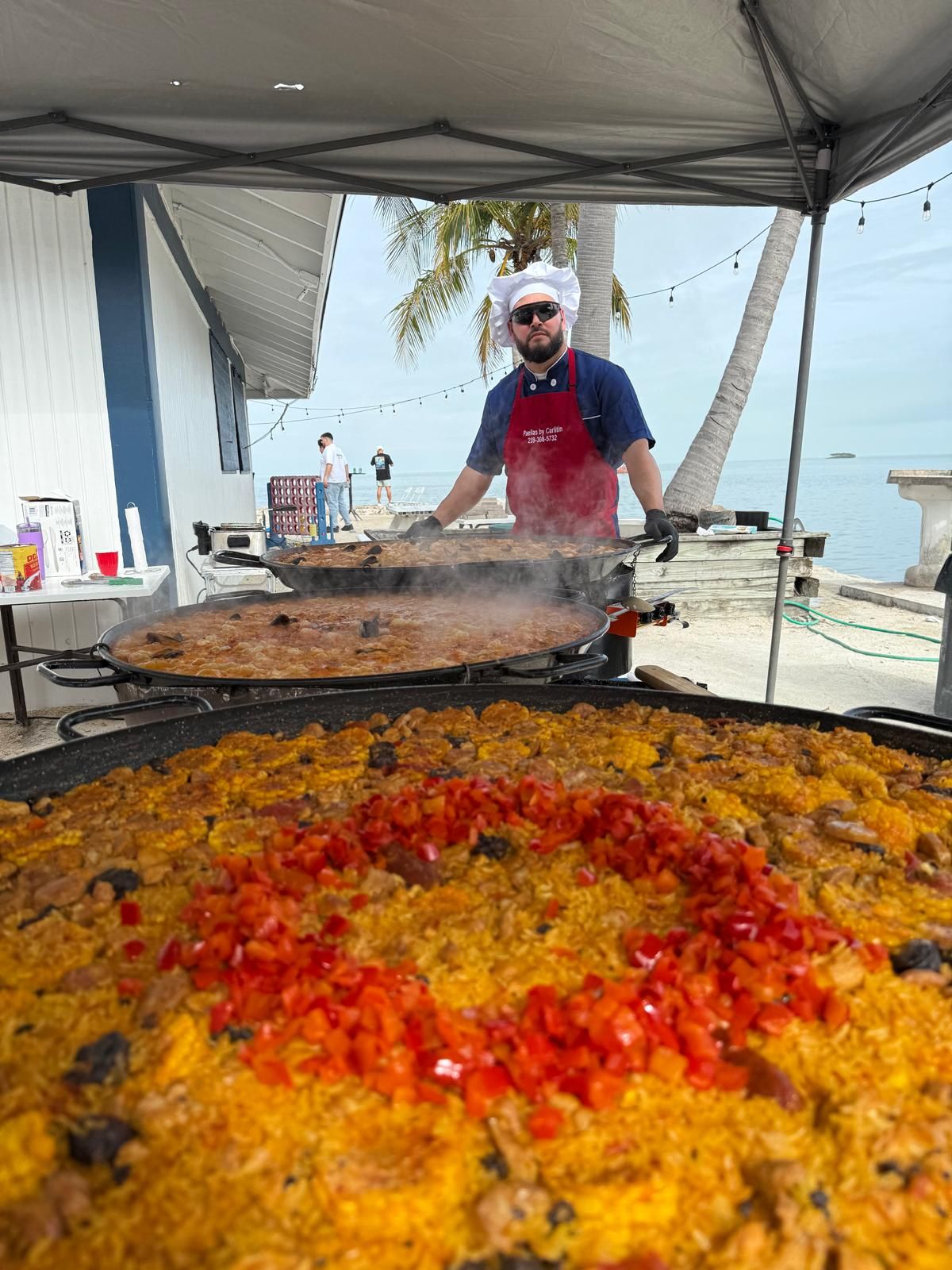 Chef Carlitin cocinando tres paellas gigantes en vivo frente al mar en un evento