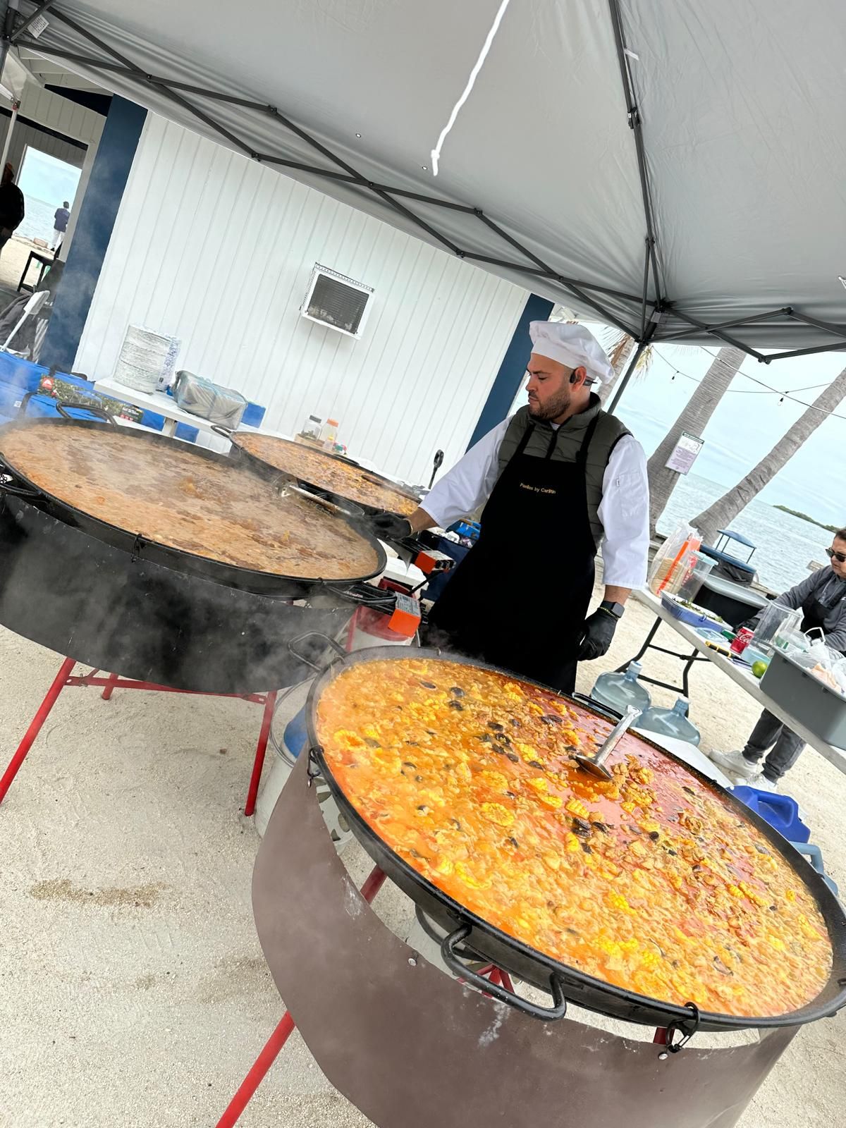 Chef removiendo dos paelleras gigantes en la playa